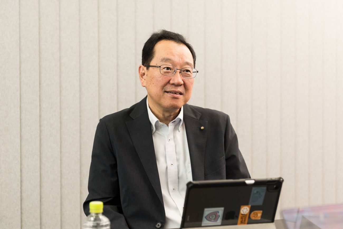 スズキ株式会社シニアフェロー鵜飼芳広氏、1983年入社。1993年から8年間アメリカのIT部門に駐在。2019年にIT本部長、2022年に常務役員を経て、2025年4月より現職